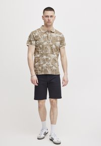 Brun polo skjorte med palmetre mønster, beige krage og korte ermer, parret med mørke shorts og hvite sokker, og svarte og hvite sko.