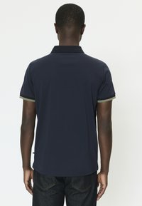 Polo de manga corta azul marino con tejido texturizado. Presenta detalles en contraste verdes y beige en el cuello y las mangas.