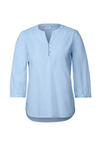Camicetta azzurro chiaro a maniche lunghe con scollatura rotonda, pattina con tre bottoni e dettagli arricciati sulle spalle. Tessuto liscio, orlo curvo.