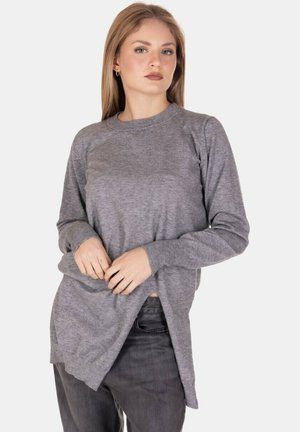 Maglietta grigia a maniche lunghe in tessuto morbido con scollo rotondo e spacchi laterali, abbinata a jeans scuri. Il modello posa con le mani sulla maglietta.