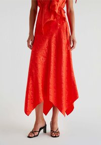 Abito midi rosso con orlo asimmetrico, realizzato in tessuto morbido che presenta un motivo sottile. Include una chiusura a lacci e dettagli a volants sovrapposti.