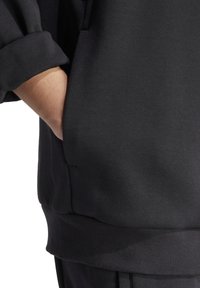 Zwarte sweatshirt met een geribbelde zoom en manchetten; heeft een zijzak met een onzichtbare hand erin gestoken. Zacht, gestructureerd materiaal.