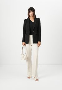 Blazer doppiopetto nero, top nero, pantaloni a gamba larga color crema, borsa beige e scarpe con punta scoperta. Tessuto morbido, vestibilità su misura, hardware minimale.
