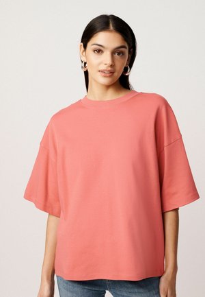 Coral oversized T-shirt made of soft fabric, featuring a crew neckline and short, wide sleeves. Smooth texture with minimal stitching details.