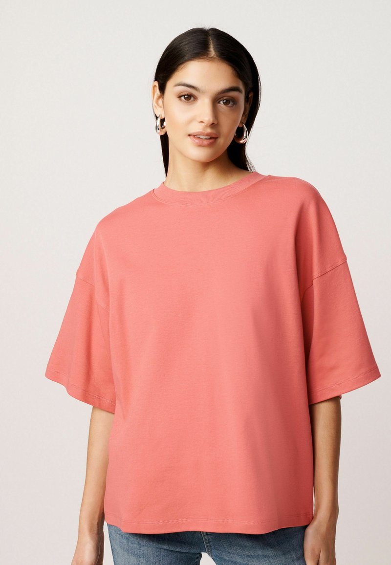 Koraalkleurig oversized T-shirt van zachte stof, met een ronde halslijn en korte, brede mouwen. Glad textuur met minimale stikseldetails.