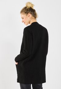 Zwarte ribgebreide cardigan met lange mouwen, zijzakken en een relaxte fit. De textuur is zacht en het ontwerp is minimalistisch.