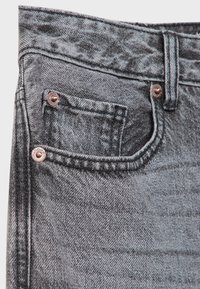Jean en denim noir avec une finition texturée, comportant une poche avant, des rivets en cuivre et des coutures contrastées le long des bords.
