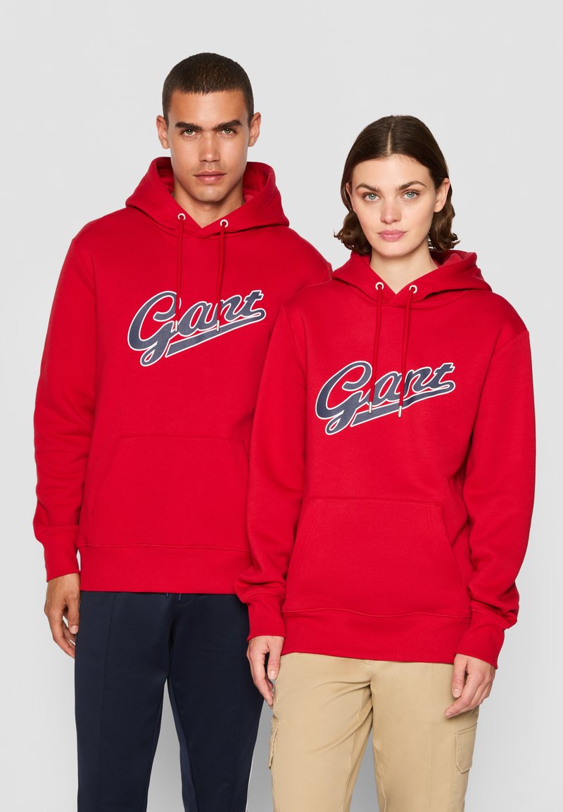 Røde hettegensere med en frontlomme og snor i hetten. Begge har "Gant"-logoet i marineblått over brystet.