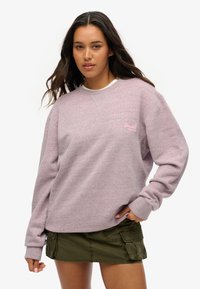 Szarylilowy sweter z okrągłym dekoltem, z ściągaczami na mankietach oraz małym logo na piersi. W zestawie z zieloną spódnicą w stylu cargo.