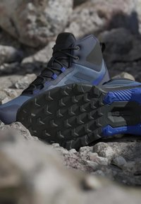 Blå och svarta vandringskängor med robusta sulor som vilar på stenig terräng, vilket framhäver mönstret på sulan och stöd för fotlederna.