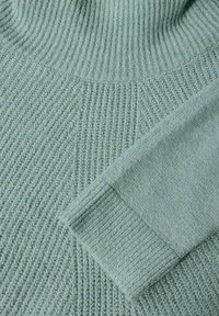 Light green knitted sweater with ribbed texture, featuring a high neckline and a cuffed sleeve showcasing a soft, cozy fabric.