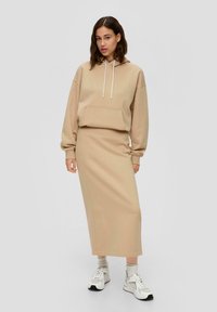 Beige hoodie met een voorzak en een trekkoord, gecombineerd met een bijpassende lange rok, gedragen met witte sneakers en lichte sokken.