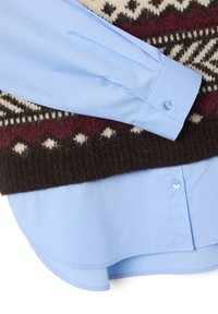 Hellblaues Hemd mit langen Ärmeln, getragen unter einem dunkelbraunen Pullover mit einem cremefarbenen und maroonfarbenen geometrischen Muster. Strukturiertes Wollmaterial.