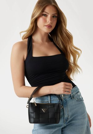 Borsa a tracolla intrecciata nera con hardware e logo oro, dotata di un manico corto. Il modello indossa un top nero a fascia e jeans azzurri chiari.