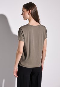 Olivově zelené tričko s krátkým rukávem, měkká látka, kulatý výstřih, uvolněný střih, boční rozparky, jednoduchý design, nošeno s černými širokými kalhotami.