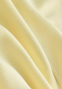Tissu jaune clair avec une texture douce et lisse, présentant des plis délicats et un motif de tissage uniforme. Idéal pour des vêtements ou de l'ameublement.