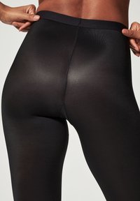 Leggings noirs extensibles avec une texture lisse et une taille haute, conçus pour un ajustement près du corps et un aspect sans couture.
