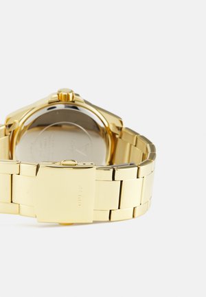 Gouden metalen polsbandhorloge met een geschakelde band, ronde kast en een sluiting. Gepolijste afwerking met zichtbare branding op de sluiting en een gladde textuur.