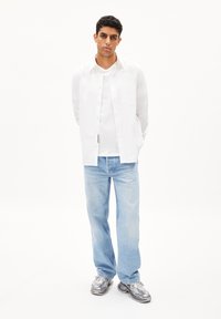 Camicetta bianca sopra una T-shirt bianca, abbinata a jeans azzurri chiari e sneakers grigie; vestibilità moderna e stile casual.
