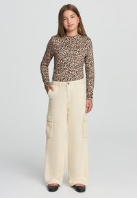 Bluzka z długim rękawem w wzór lamparta o dopasowanym kroju; beżowe spodnie cargo z szerokimi nogawkami i kieszeniami, z zapięciem na guzik. Czarne buty.