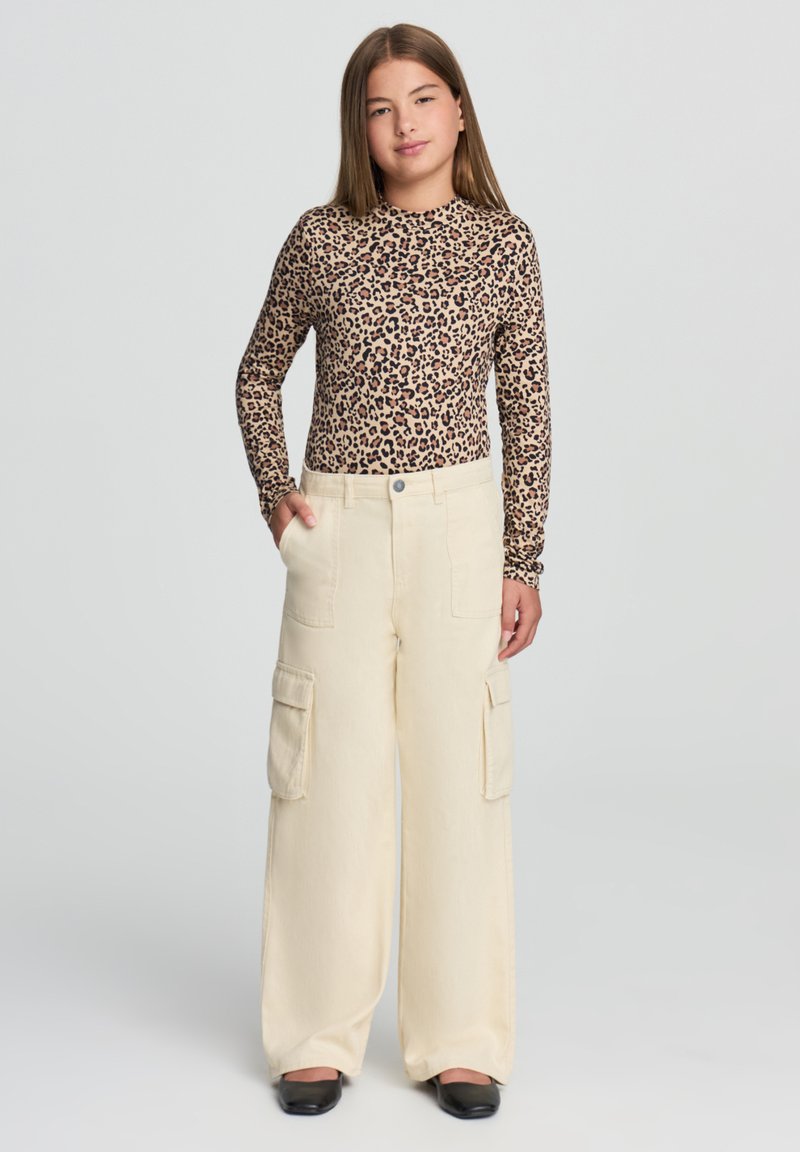 Bluzka z długim rękawem w wzór lamparta o dopasowanym kroju; beżowe spodnie cargo z szerokimi nogawkami i kieszeniami, z zapięciem na guzik. Czarne buty.