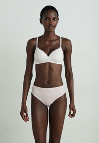 Hvit blonde bralette med justerbare stropper og myke kopper, kombinert med lyserosa høyhåndterte truser; glatt tekstur, minimalistisk design.