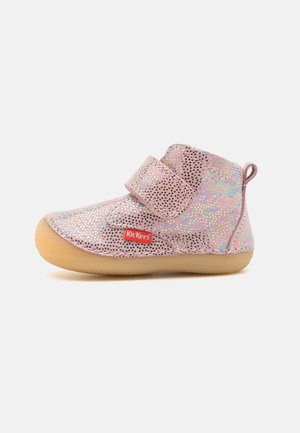 Chaussure rose pour tout-petit avec motif holographique de petits triangles, bride Velcro, semelle beige et logo Kickers rouge sur le côté.