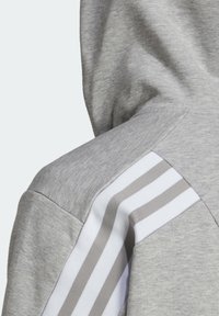 Tessuto di felpa grigio con superficie strutturata. Caratterizzato da un cappuccio e strisce bianche con accenti grigi sulle spalle.