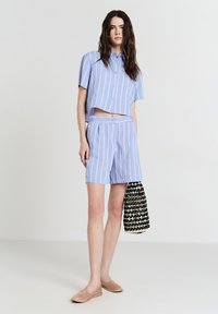 Camicia azzurra corta con bottoni e strisce verticali bianche, abbinata a pantaloni corti azzurri. Presenta una borsa texturizzata bianca e nera.