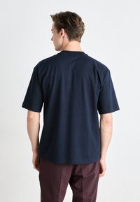 Ναυτικό βαμβακερό μπλουζάκι κοντομάνικο, χαλαρή γραμμή και κλασικός λαιμός crew. Λείο ύφασμα χωρίς εμφανή λογότυπα ή γραφικά.