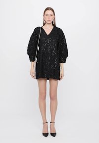 Black sequin mini dress with a V-neck, puffed sleeves, and textured fabric. Paired with black pointed-toe heels and a small metallic purse.