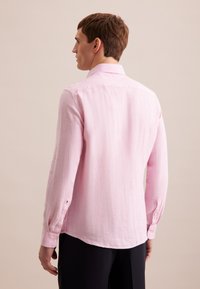Camicia a maniche lunghe di colore rosa chiaro realizzata in un tessuto texturizzato, con colletto a bottoni, bottoni sui polsini e orlo curvo.