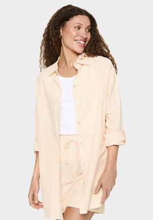 Chemise rayée à boutons dans des tons pastel orange et blanc. Caractérisée par une coupe décontractée, des manches retroussées et un col, associée à un débardeur blanc.