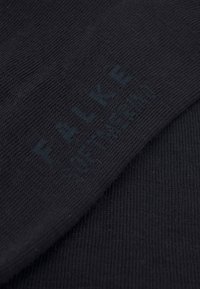 Chaussettes noires en tissu côtelé, offrant une texture douce. Imprimées avec "FALKE" en bleu foncé à la surface.