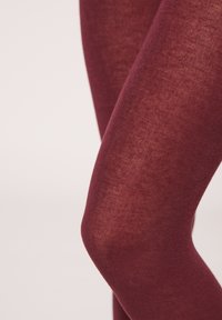 Collant bordeaux realizzati in un materiale morbido ed elastico, con una texture liscia, design aderente e una leggera lucentezza.