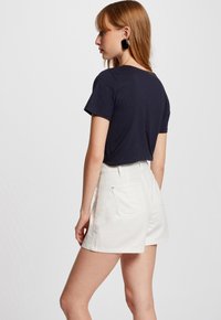 Camiseta de manga corta en color marino combinada con pantalones cortos blancos de cintura alta. Los pantalones cortos tienen bolsillos laterales y dos bolsillos traseros, con una textura suave.