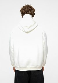 Witte hoodie met een trekkoord capuchon en geribde zoom. Heeft een gladde textuur en een losse pasvorm. Gecombineerd met donkere denim broeken.