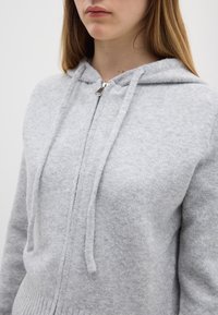 Felpa con cappuccio in lana grigia con zip, coulisse e orlo a coste, caratterizzata da una zip argento e una superficie morbida e testurizzata.