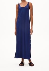 Robe maxi marine avec un décolleté en cœur, sans manches, fentes sur les côtés et un tissu lisse et léger. Portée avec des sandales plates sombres.