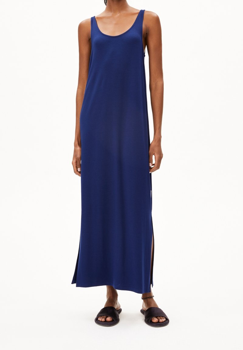 Robe maxi marine avec un décolleté en cœur, sans manches, fentes sur les côtés et un tissu lisse et léger. Portée avec des sandales plates sombres.