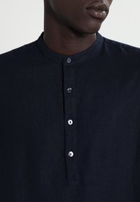 Camicia in lino blu navy con colletto alla francese, dotata di una fila di bottoni e bottoni chiari a contrasto, che mette in risalto un tessuto testurizzato e traspirante.