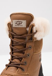 Waterdichte bruine leren boot met een fluffy crème kraag. Bevat bruine veters en metalen oogjes. Inclusief een UGG-label op de tong.