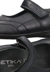 Zapatos infantiles de cuero negro con cierre de velcro, punta redondeada, acabado texturizado y plantilla acolchada para mayor comodidad.