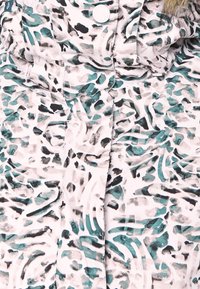 Gros plan d'une veste avec un motif animal abstrait vert, noir et gris et un bouton blanc visible en haut au centre.