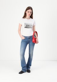 T-shirt blanc à manches courtes avec un imprimé photo en noir et blanc, associé à un jean en denim bleu évasé et un sac à main rouge.