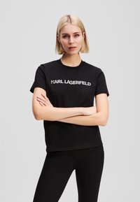 T-shirt in cotone nero con la scritta "KARL LAGERFELD" in lettere bianche sul petto. Maniche corte e scollo rotondo classico.