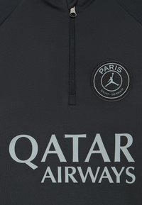 Sort, langermet treningsgenser med glidelås i halsen, med en rund PSG-logo og sølvfarget "QATAR AIRWAYS"-tekst tydelig vist.
