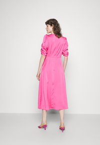 Vestido midi de cetim rosa com mangas bufantes, cintura ajustada e saia rodada. Combinado com saltos abertos rosa, mostrado de costas.