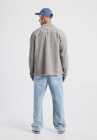 Gray corduroy jacket with a collar, button cuffs, and casual fit, paired with light blue denim jeans and a blue cap.