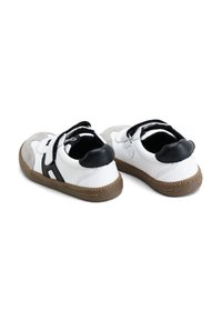 Zapatos de cuero blanco con acentos negros, detalles en gamuza gris y suelas de goma marrón. Cuentan con correas de gancho y bucle para un fácil calzado.